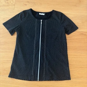 Prickig topp med dragkedja - Snygg svart topp med vita prickar och en dragkedja framtill. 