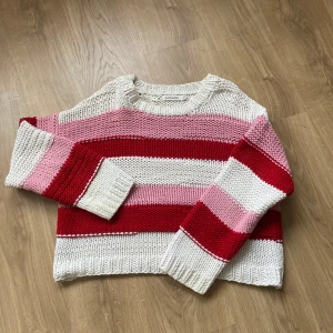Randig stickad tröja i rött och rosa - Säljer en mysig stickad tröja med breda ränder i rött, rosa och vitt. Tröjan har en avslappnad passform och långa ärmar, perfekt för kyligare dagar. Den är både stilren och bekväm, ett måste i garderoben!