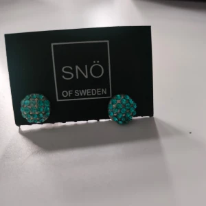 Turkosa örhängen från SNÖ of Sweden - Snygga turkosa örhängen från SNÖ of Sweden. Dessa små, runda örhängen är täckta med glittrande stenar som ger en elegant touch. Perfekta för att lysa upp vilken outfit som helst. Oanvända.