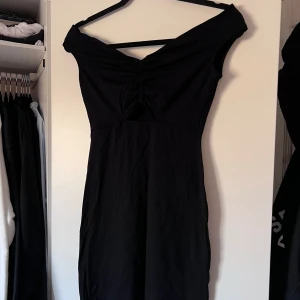 Svart klänning med offshoulder-design - Snygg svart klänning med offshoulder-design och rynkad detalj framtill. Perfekt för en stilren look. Klänningen har en smickrande passform och är tillverkad i ett mjukt material. Använd 1 gång. Önskar du veta exakta mått? Tveka inte att höra av dig!