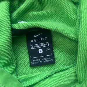 Grön hoodie från Nike - Säljer en grön Nike hoodie med Dri-Fit teknologi. Den har en stor svart Nike-logga på framsidan och en praktisk magficka. Perfekt för träning eller vardagsbruk.