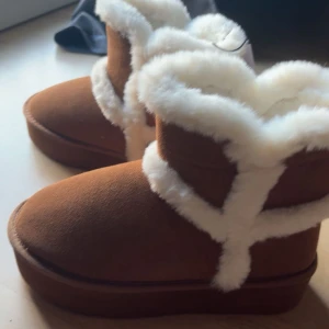 Bruna boots med vit päls - Mysiga bruna boots med vit pälsdetalj. Perfekta för kalla dagar med sin varma och bekväma design. De har en rund tå och är gjorda i ett mockaliknande material.