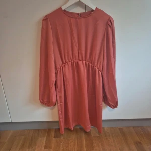 Rosa klänning med lång ärm - Söt klänning med lång ärm och rund hals. Klänningen har en lätt rynkad midja och stängs med en knapp i ryggen. Perfekt för en stilren och bekväm look.