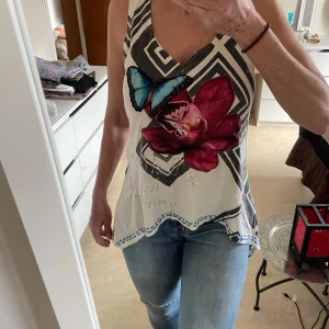 Mönstrad ärmlös topp från Desigual - Säljer en unik ärmlös topp från Desigual med   mönster blommor framme  som är sydda på . På insidan står . Texten 'Say something nice!!' finns på baksidan. Perfekt för dig som vill sticka ut!storlek one size motsvarande seller medium, jag på bild har medium i storlek.
