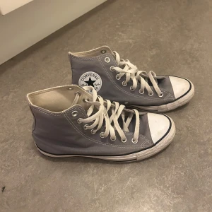 Grå höga sneakers från Converse - Säljer ett par klassiska grå höga Converse sneakers med vit sula och snörning. Skorna har den ikoniska Converse-loggan på sidan och är perfekta för en avslappnad stil.