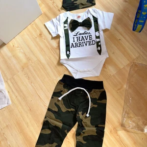 Kamouflagefärgade byxor för barn - Säljer ett par coola kamouflagefärgade byxor för barn med snörning i midjan. Perfekta för små äventyrare! Byxorna har en bekväm passform och matchar fint med den medföljande bodyn och mössan. Nyskick! 