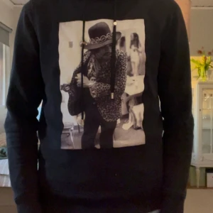 Svart hoodie från Limitato med Jimi Hendrix-tryck - Säljer en svart hoodie från Limitato med ett coolt tryck av Jimi Hendrix på framsidan. Tröjan är tillverkad i 100% bomull och har en bekväm passform med justerbar huva. Perfekt för dig som vill ha en unik och stilren look. Det är defekt vid armbågarna men det påverkar ej passformen o h ser snyggt ut. Hör av er vid fler bilder och intressen!