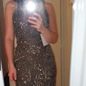 Glittrig långklänning med paljetter - Snygg glittrig långklänning med intrikata paljettmönster. Klänningen har smala axelband och en v-ringad.