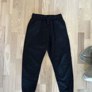 Svarta mjukisbyxor med snörning - Säljer ett par bekväma svarta mjukisbyxor med elastisk midja och snörning. Perfekta för en avslappnad stil. Byxorna har en loose passform och är gjorda i mjukt material.