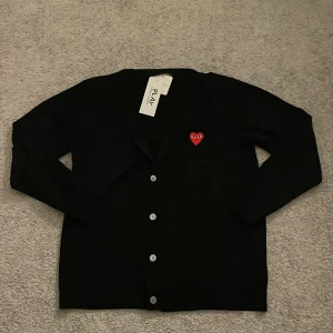 Svart cardigan från Comme des Garçons - Säljer en stilren svart kofta från Comme des Garçons med det ikoniska röda hjärtat med ögon på bröstet. Köpt i Japan nypris runt 2200kr.