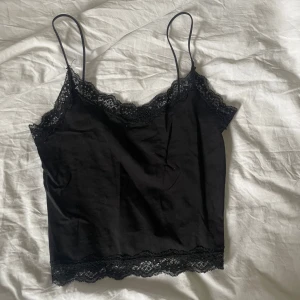 Svart linne från Only - Säljer ett stilrent svart linne från Only med spetsdetaljer vid halsringning och nederkant. Linnet har tunna axelband och är perfekt för lager-på-lager eller som det är. Ett måste i garderoben för en chic look!