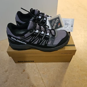 Salomon Grivola GTX W - Säljer ett par Salomon Grivola GTX W i svart och grått. Skorna har GORE-TEX för vattentäthet och en robust sula för bra grepp. Perfekta för utomhusaktiviteter med snörning för säker passform.