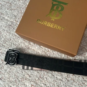 Svart bälte från Burberry - Snyggt svart bälte från Burberry med ett stilrent rutigt mönster. Bältet har ett iögonfallande spänne med Burberrys ikoniska logotyp i silver. Perfekt för att ge en lyxig touch till din outfit. Inte äkta men box o allt är med har aldrig användts