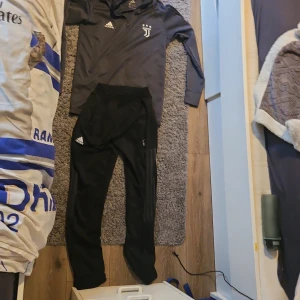 Svarta träningsbyxor från Adidas - Säljer ett par svarta träningsbyxor från Adidas med elastisk midja och dragkedja vid fickorna. Perfekta för sport och träning. Byxorna har Adidas-loggan på ena benet och tre ränder längs sidan.