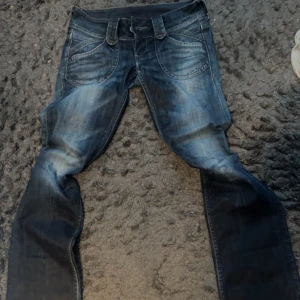 Blå bootcut low waist jeans från Pepe Jeans, aldrig använda och säljer då de tyvärr är för små för mig - Snygga blå jeans från Pepe Jeans med en klassisk femficksdesign och coola slitningar. De har en bootcut passform och är perfekta för en avslappnad stil. Jeansens detaljer inkluderar broderade bakfickor och en bekväm midja.
