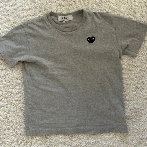 Grå t-shirt från Play - Säljer en t-shirt från CDG Play med ett litet svart hjärta med ögon på bröstet. T-shirten är storleken Large, men sitter som xs.