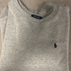 Grå tröja från Polo Ralph Lauren - Säljer en stilren grå tröja från Polo Ralph Lauren. Tröjan har en klassisk rund halsringning och det ikoniska logotypbroderiet på bröstet. Perfekt för en avslappnad och snygg look. Pris kan diskuteras vid snabb affär
