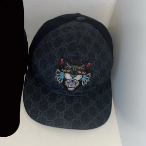 Gucci keps - Snygg svart keps med ett broderat kattmotiv framtill. Kepsen har ett diskret mönster och justerbar passform. Perfekt för att ge din outfit en cool touch. Extremt svår få tag på