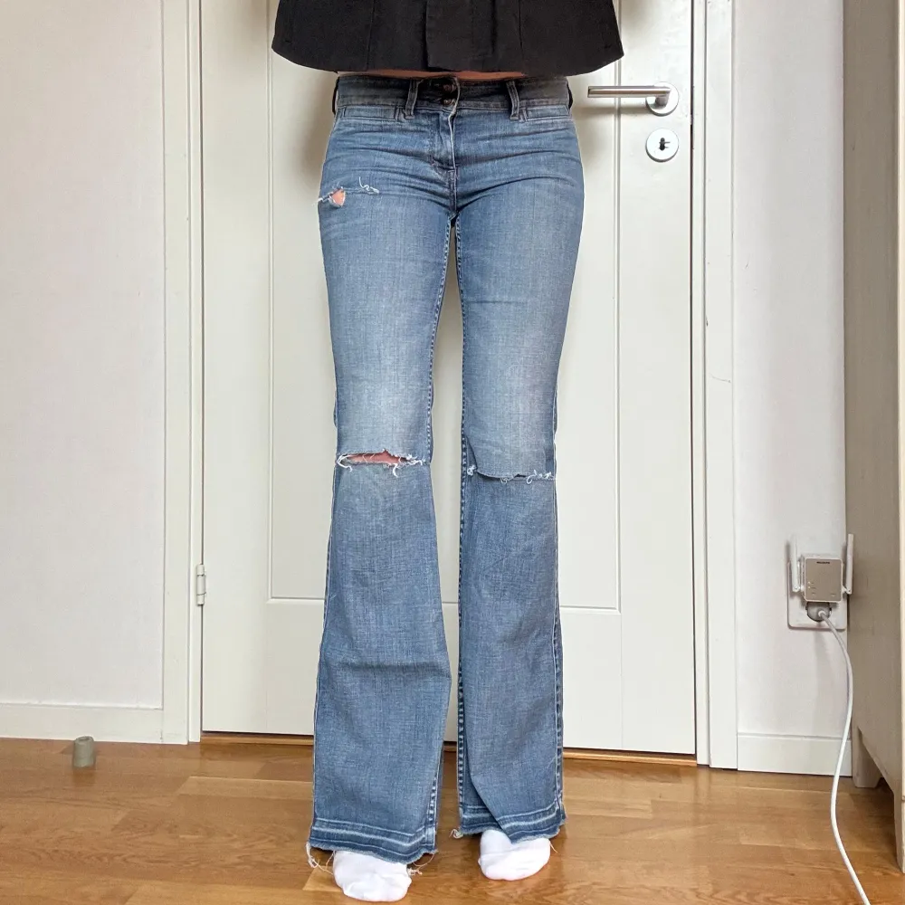 Snygga blå bootcut jeans med slitningar på låren och hål på knäna. Jeansen har en lågmidjad passform och är tillverkade i ett bekvämt denimtyg. Storlek 28x32. Jag är ca 177 cm. Midjemåttet är ca 80 cm, innerbenslängden är ca 88 cm och grenmåttet är ca 21 cm. En liten defekt på baksidan som tidigare varit ett hål som är igen sytt, syns på sista bilderna.. Farkut & Housut.
