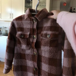 Brun och beige rutig overshirt - Säljer en snygg brun och beige rutig overshirt med knappar framtill. Jackan har långa ärmar. Perfekt för lager-på-lager-stil.