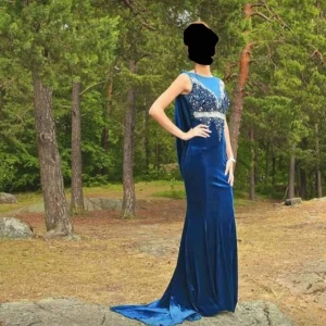 Blå långklänning med paljetter - Elegant blå långklänning med glittriga paljettdetaljer på överdelen. Klänningen har en ärmlös design och ett flytande fall som ger en vacker siluett. Perfekt för speciella tillfällen. I marin blå sammet . Väldigt bekväm. Storlek 34. 