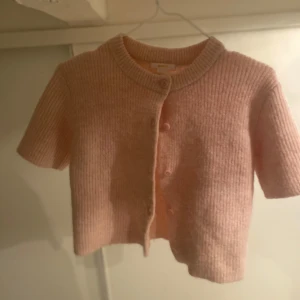 Rosa ribbad kofta från Gina Tricot - Säljer en söt rosa ribbad kofta från Gina Tricot. Koftan har korta ärmar och knappar framtill. Perfekt för en stilren och bekväm look. Passar bra till både jeans och kjol. 🌸