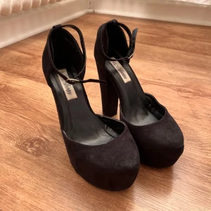 Svarta mocka pumps från Nelly (NLY Shoes) - Snygga svarta pumps i mocka från NLY Shoes med hög klack och ankelrem. Perfekta för en elegant look. De har en rund tå och en stabil klack för extra komfort.