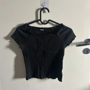 Svart ribbad topp - Snygg svart ribbad topp med korta ärmar och vågig kant. Perfekt för en stilren look.