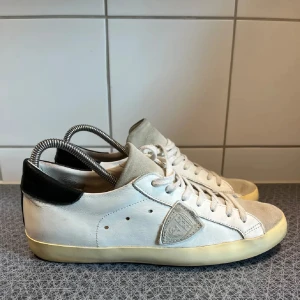 Philippe Model sneakers - Snygga vita philippe model sneakers  med svarta detaljer och snörning. Skorna har en klassisk design med en bekväm passform och en diskret logga på sidan. Perfekta för en stilren look. Priset kan diskuteras