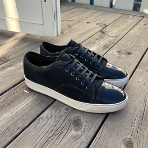 Lanvins uk 10 passar 44/45 - Snygga mörkblå sneakers från Lanvin med en kombination av mocka och glansigt material på tån. Skorna har en vit sula och klassisk snörning. Perfekta för en stilren look. Topp skick inget og tillkommer kvitto finns ej, priset går att diskutera vid snabb affär 