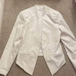 Vit kavaj från C - Elegant vit kavaj från märket C. Den har en stilren design med långa ärmar och en öppen front utan knappar. Perfekt för en chic och sofistikerad look.