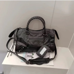 Svart balenciagaliknande väska  - Snygg svart väska💕. Väskan har dragkedja och dekorativa detaljer framtill. Perfekt för att bära med sig det nödvändigaste med stil.