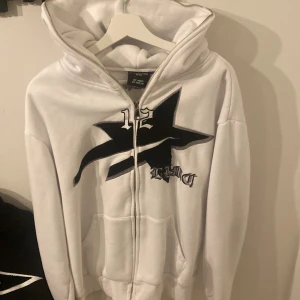 Vit hoodie med svart tryck från lukamachán - Säljer en vit hoodie från lukamachán med ett stort svart tryck på framsidan. Hoodien har dragkedja och en rymlig huva. Perfekt för en avslappnad stil.