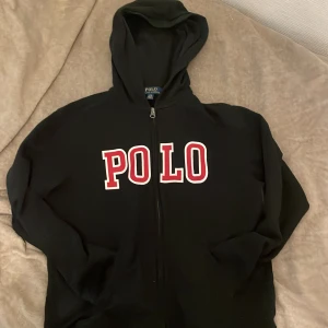 Svart hoodie från Polo Ralph Lauren - Svart hoodie från Polo Ralph Lauren med stor vit och röd POLO-logga på bröstet. Tröjan har dragkedja framtill, huva och långa ärmar. Perfekt för en chill och sportig look. Lite liten i storleken, pris kan diskuteras😀 hör av er om några frågor mvh Axel🤩
