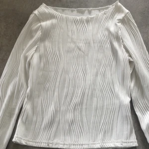 Vit långärmad topp med struktur - Säljer en vit långärmad topp med vågiga strukturränder. Tröjan har en rak passform och är tillverkad i ett mjukt material som känns skönt mot huden. Perfekt för dig som gillar stilrena plagg med en twist.