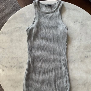 Grå ribbad klänning från SHEIN - Grå ärmlös ribbad klänning från SHEIN i storlek S. Klänningen är kroppsnära med rund halsringning och har en enkel, stilren design. Tillverkad i mjukt och stretchigt material som sitter snyggt på kroppen. Perfekt för en clean och chill look. Har ett litet hål som finns på sista bilden