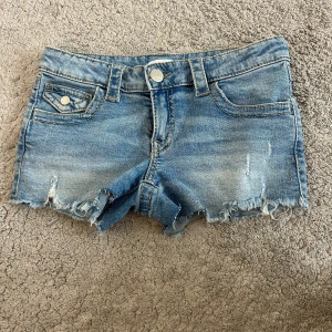 Blå jeansshorts från Gina Tricot - Snygga blå jeansshorts från Gina Tricot med slitna detaljer och fransig kant. Klassisk femficksmodell med knapp och dragkedja framtill samt coola bakfickor med lock. Perfekta för varma dagar och en avslappnad stil. Väldigt low waist!!