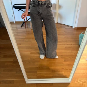 Gråa wide jeans med hög midja - Säljer ett par gråa jeans med hög midja och breda ben. Jeansen har klassisk femficksdesign, dragkedja och knapp framtill. Materialet är kraftig denim och passformen är loose och relaxed. Perfekta för en chill och trendig look.