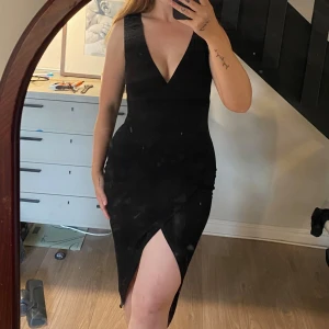 Svart klänning med v-ringning och slits - Snygg svart omlott-klänning med djup v-ringning och en hög slits framtill. Klänningen är ärmlös och har en tight passform. 