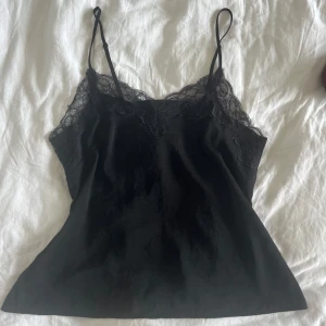 Svart linne med spets - Svart linne från H&M med tunna axelband och snygga spetsdetaljer längs urringningen. Perfekt som fint nattlinne eller topp till jeans/kjol!