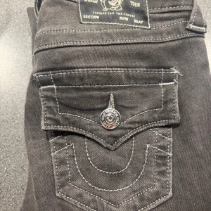 True Religion Becca Bootcut Jeans - Snygga svarta True Religion Becca jeans med bootcut och coola kontrastsömmar. Klassisk fickdesign med lock och silverfärgad knapp. Midwaist passform och tillverkade i mjukt jeanstyg. Perfekta för dig som gillar streetstyle och vill sticka ut. Knappt använda!! Snabb affär sänker jag priset!! 