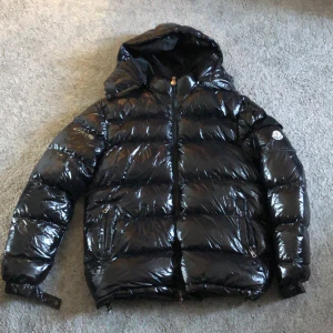 Svart Moncler maya L passar M - Säljer en svart Moncler maya med huva och dragkedja. Jackan har Moncler-logga på ärmen, två fickor med dragkedja och en riktigt fet dunfyllning som håller dig varm. Perfekt för kalla dagar när du vill se både stylish och chill ut. Från Turkiet har använts 3 gånger