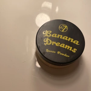 W7 Banana Dreams Loose Powder - Banana Dreams Loose Powder från W7 är ett löspuder med en gul ton som ger en matt finish och jämnar ut hudtonen. Perfekt för att sätta foundation och ge en fräsch look. Kommer i en rund plastburk med svart lock och gul text.