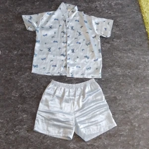 Vit skjorta med blå fjärilar - Kortärmad vit skjorta med blå och gröna fjärilar, klassisk krage och knäppning framtill. Skjortan är luftig och perfekt för varma dagar. Materialet ser ut att vara bomull eller linne, vilket gör den sval och bekväm.