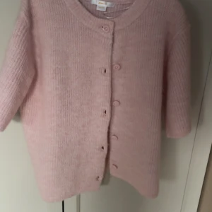 Ljusrosa stickad kofta Gina Tricot - Supermjuk ljusrosa stickad kofta från Gina Tricot med ribbad struktur och knappar framtill. Koftan har rund halsringning och trekvartsärmar, perfekt för lager-på-lager och chill vibes. 