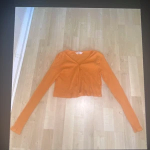 Orange croppad kofta från H&M - Snygg orange croppad kofta från H&M med lång ärm och v-ringad front. Tunn och lätt i bomullsmaterial, perfekt för lager-på-lager. Enkel att matcha med jeans eller kjol för en chill look.