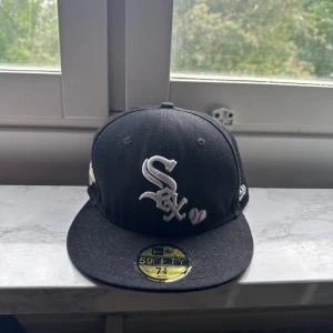 Chicago White Sox 59FIFTY keps svart 7 3/8, 58,7 cm - Snygg svart 59FIFTY keps från New Era med Chicago White Sox-logga broderad framtill i vitt. På sidan finns ett World Series 05-märke och bak står det 'Love & Hustle = Game'. Klassisk flat peak och broderade detaljer. Perfekt för dig som gillar baseball och streetwear.
