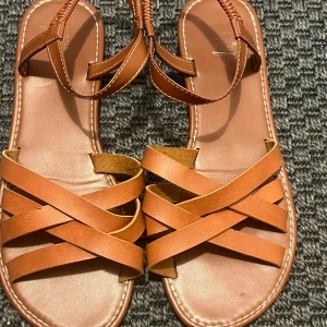 Bruna sandaler med korsade remmar - (Priset kan diskuteras🩷)Snygga bruna sandaler med flera korsade remmar och öppen tå. De har en platt sula och vita kontrastsömmar runt kanterna. Remmarna är i skinnimitation och sandalerna har en enkel, stilren look som passar perfekt till varma dagar. Den är lite förstörd på ena delen av sandalen(se bild.3✨) Däremot så är de jätte vackra inför sommaren. 🥰inte med bara det så passar de också som 40-42storlek.