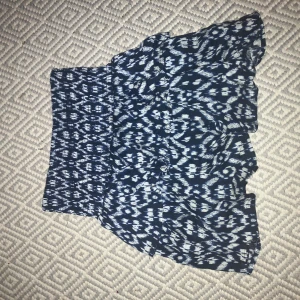 Mönstrad blåvit kortkjol med volang - Supersöt kortkjol i marinblått och vitt med ett unikt mönster och volangig nederdel. Kjolen har bred resår i midjan som sitter skönt och ger en snygg passform. Perfekt för dig som gillar en chill och trendig stil.