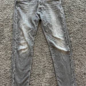 Grå tapered jeans Tapered/Mike - Snygga grå jeans i tvättad look från Tapered/Mike. Modellen är tapered med smalare ben och klassiska femficksdetaljer. Jeansen har guldfärgade nitar och dragkedja. Perfekta för dig som gillar en modern och avslappnad stil. 29/30. Den har ett litet hål vid knäskålen 